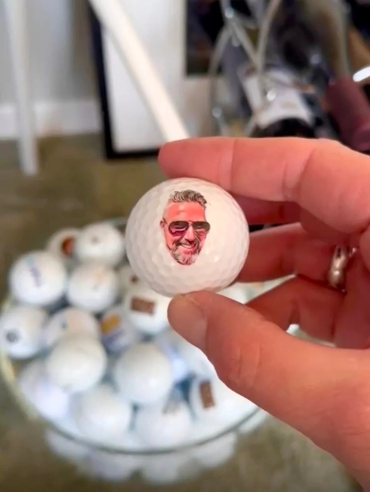 Hand houdt een golfbal met een gezicht erop boven een bak bedrukte ballen