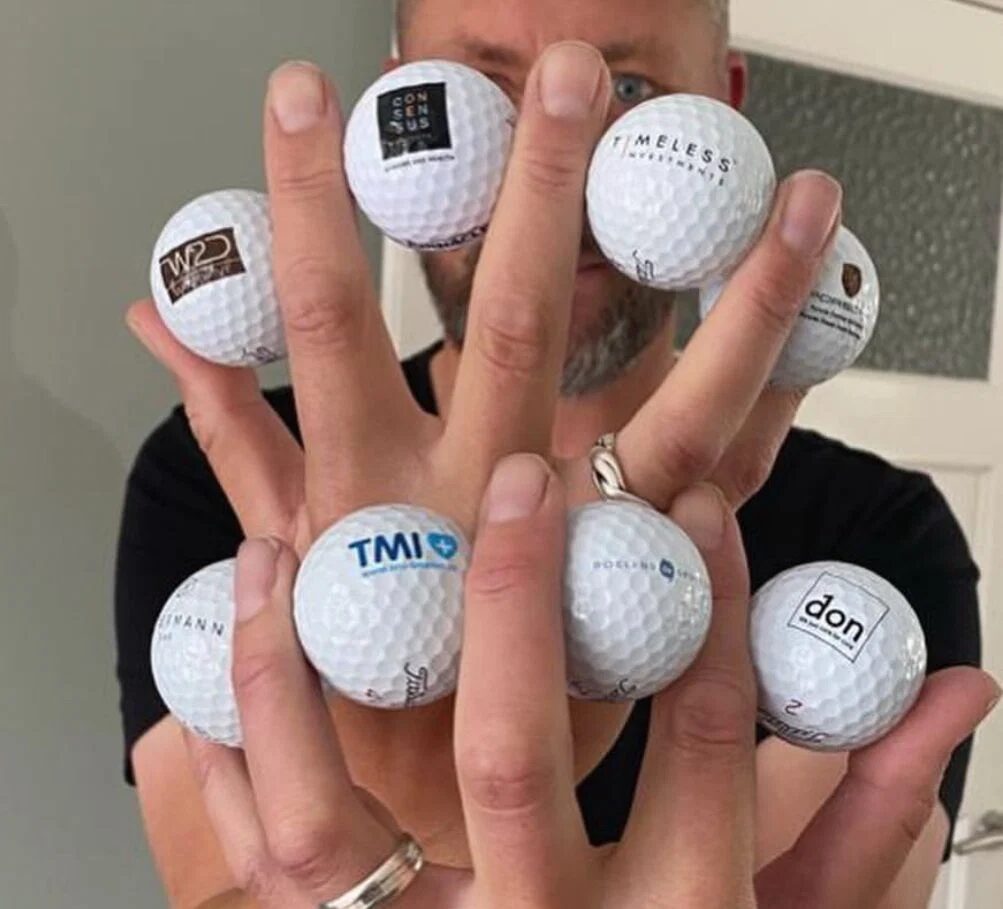Twee handen vol bedrukte golfballen met verschillende bedrijfslogo’s
