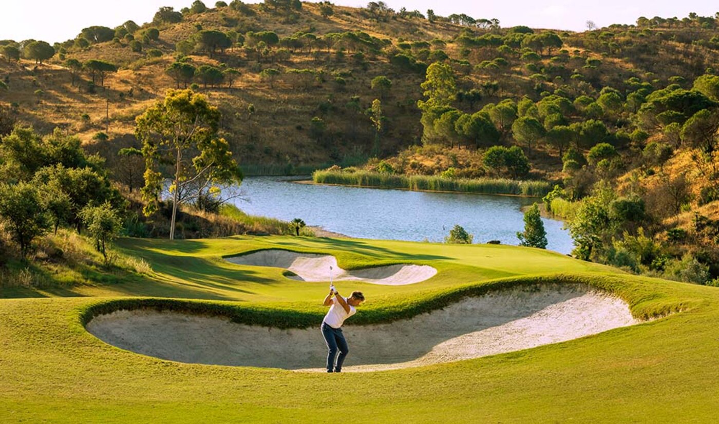 Golfer slaat uit de bunker op een zonnige golfbaan met uitzicht op een meer